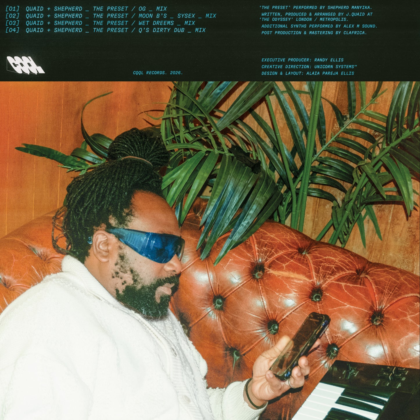 Man with sunglasses using a phone on a brown leather couch with plants in the background